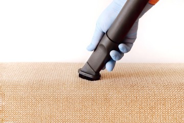 A female hand in a glove vacuums the surface of the sofa. The concept of home cleaning,...