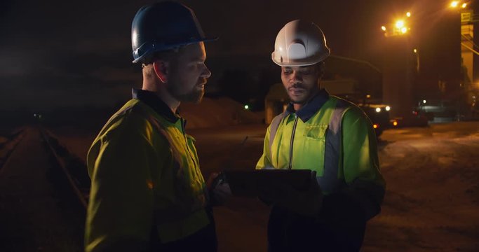 Foreman and engineer discussing production plan over tablet at concrete plant late at night