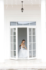 Fototapeta na wymiar Beautiful woman bride in a white dress sitting in a house near a large window