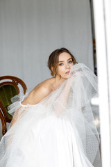 Portrait of a beautiful bride woman who is sitting on a chair and holding her dress