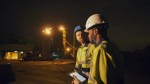 Portrait of two diverse industrial workers talking at construction site late at night