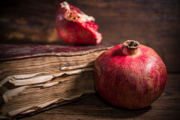 Juicy red pomegranates with aged book on wooden background