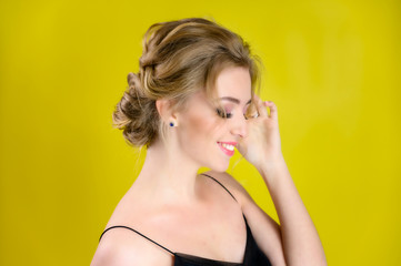 Glamorous beauty portrait side view of a pretty blonde model with excellent makeup and a beautiful hairstyle on a yellow background in the studio. The concept of cosmetics, fashion and style.