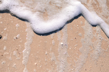 Wet sand and sea foam on the beach, sea waves. Summer time, vacation travel concept. Copy space for your text