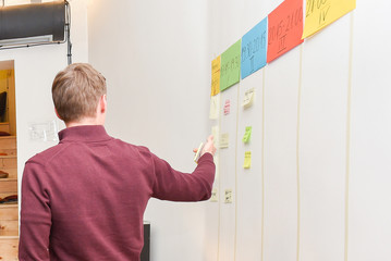 Brown haired man standing and pointing to whiteboard teaching agile scrum technique and methodology during the workshop inside of the office space 
