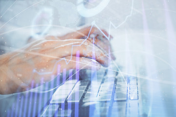 Multi exposure of graph with man typing on computer in office on background. Concept of hard work. Closeup.