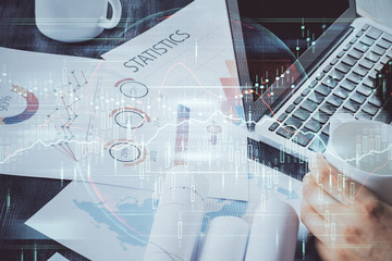 Double exposure of stock graph with businessman typing on computer in office on background. Concept of hard work.