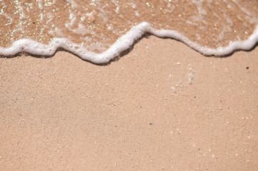 Fototapeta na wymiar Wet sand and sea foam on the beach, sea waves. Summer time, vacation travel concept. Copy space for your text