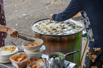 Woman making tiny shrimp pancake at Vietnamese street food vendor