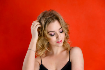 Glamorous beauty front view portrait of a pretty model with blond hair with great makeup and a beautiful hairstyle on a red background in the studio. The concept of cosmetics, fashion and style.