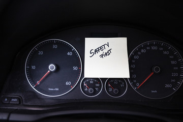 Writing safety first on memo post reminder. Text on sticky paper inside car dashboard.