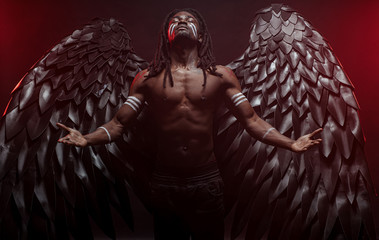 shirtless dark angel isolated in red smoky space, young muscular angel come down from heaven for...