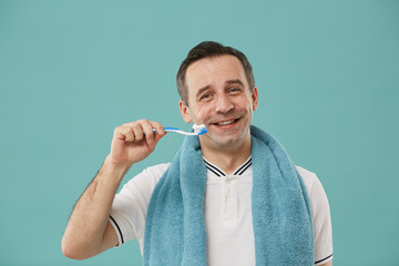 Waist up portrait of happy middle aged man holding toothbrush and smiling at camera while enjoying...