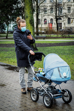 Handsome young European man in winter clothes on the street with a medical face mask on and baby carriage. 35-year-old male in a respirator to protect against infection with  coronavirus