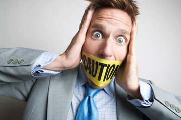 Businessman gagged with yellow caution tape holding his head in his hands