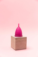 Menstrual Cup on a pedestal on pink background. Copy space. Woman hygiene protection. Symbol.