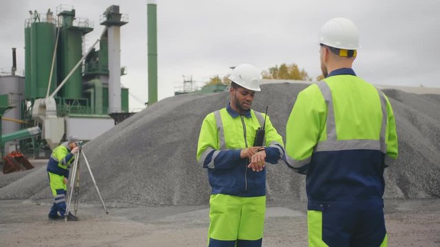 Foreman instructing industrial worker standing outdoors at asphalt and cement factory