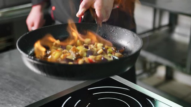 Chef cooking vegetable in frying pan on burning fire slow motion. Close up shot on 4k RED camera