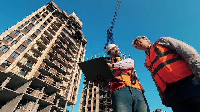 Construction contractor working on a construction site. Men stand on a site, working with a laptop.