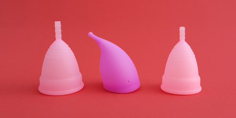 three different pink reusable silicone menstrual cups isolated on red background. Concept of feminine hygiene, gynecology, health.