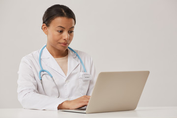 Portrait of beautiful female doctor using laptop while sitting against white background, copy space