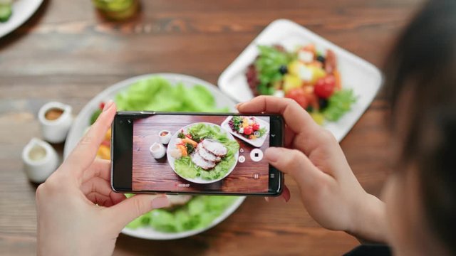 Top view female taking photo of food on serving plate using smartphone. Shot with RED camera in 4K