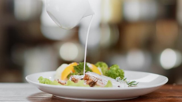 Pouring cream sauce on meat in plate with vegetable slow motion. Close up shot on 4k RED camera