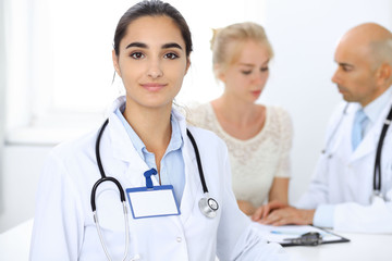 Doctor woman in clinic with colleagues at the background. Hispanic or latin american staff in medicine