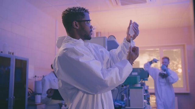 African-american scientist or graduate student in lab coat and protective wear works in modern laboratory