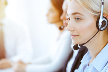 Group of diverse phone operators at work in sunny office. Handsome business woman with headphones consulting clients. Call center and business people concept