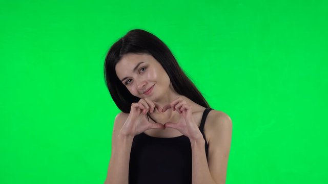 Young girl smiles and showing heart with fingers then blowing kiss. Green screen