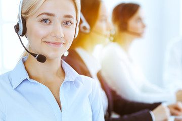 Group of diverse phone operators at work in sunny office. Handsome business woman with headphones...