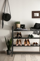 Black shelving unit with shoes and different accessories near white wall in hall
