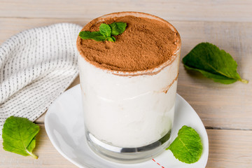 Tiramisu dessert in a white glass with mint leaves