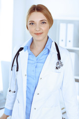 Young woman doctor at work in hospital looking at camera. Blue colored blouse of therapist looks good. Medicine and healthcare concept