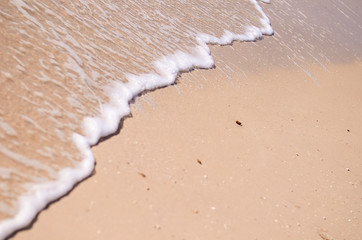 Wet sand and sea foam on the beach, sea waves. Summer time, vacation travel concept. Copy space for your text