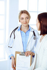 Fototapeta premium Young woman doctor and patient at medical examination at hospital office. Blue color blouse of therapist looks good. Medicine and healthcare concept