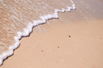 Wet sand and sea foam on the beach, sea waves. Summer time, vacation travel concept. Copy space for your text
