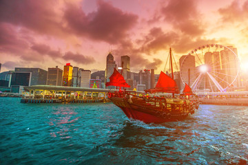 Sunset red-sail junk boat with skyscrapers and building of Hong Kong city skyline in China.