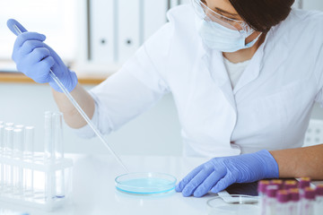 Close-up of professional female scientist in protective eyeglasses making experiment with reagents...