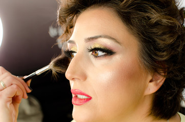 Obraz premium Make-up artist working with brush on model face. Side portrait of young woman in beauty studio interior. Close up of beautiful young brunette female model getting blush with big cosmetic brush