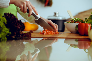 Unknown human hands cooking in kitchen. Woman slicing red tomatoes. Healthy meal, and vegetarian food concept