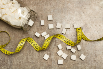 Terrones en cubos de azúcar blanca junto a una cinta métrica sobre una tabla gris rústica. Vista superior. y de cerca. Copy space. Concepto: Salud Dieta para controlar el peso.