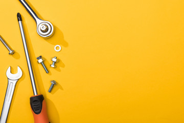 Top view of wrenches, screwdriver and bolts on yellow background