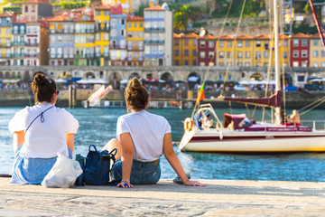 women sitting on a pier in a harbor and enjoying view of Porto, Portugal. back view girls....