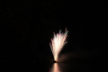 Distant shot of fireworks in the skies reflected in the waters
