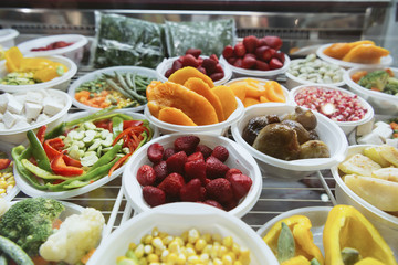 A variety of freshly frozen fruits lie on a freezer display case.