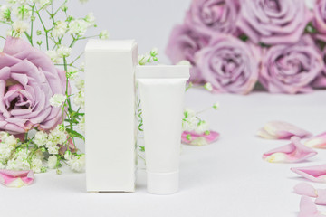 Plastic cosmetic tube and cardboard box on a white background with flowers roses and petals, mockup, beauty product and spa concept