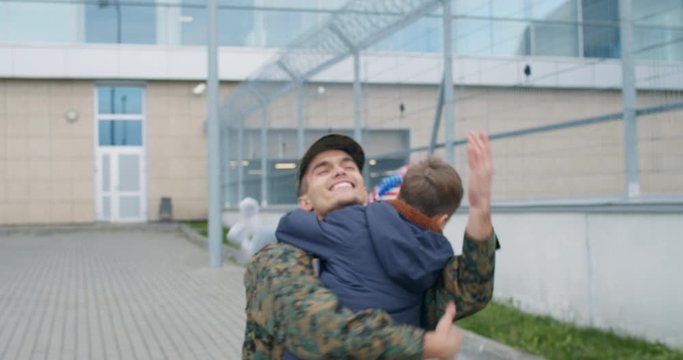 Son with USA flag running into father soldier embrace.