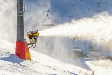 Operating artificial snow cannon near piste making snowy powder.Ski lift ropeway on hilghland...